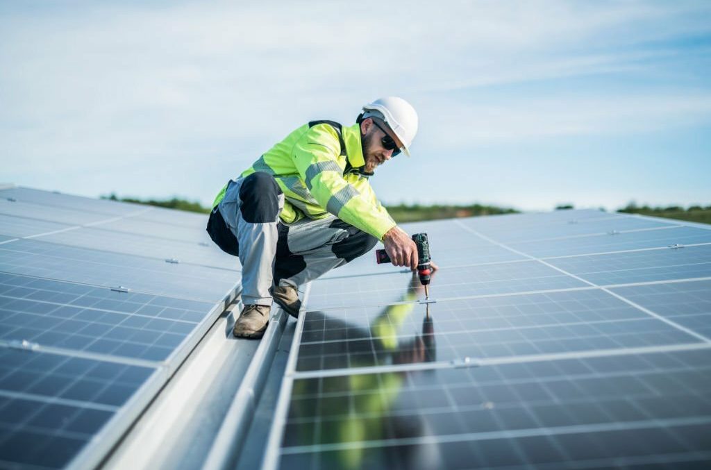 Worker in safety gear inspecting solar panels on a roof.